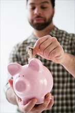 Portrait of man holding piggy ban and putting money inside