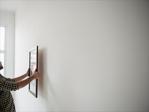 Side view of man hanging picture on wall