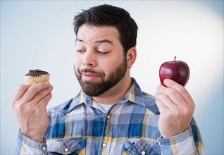 Portrait of uncertain man holding apple and cupcake