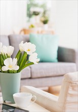 Vase with flowers and digital tablet on coffee table by sofa