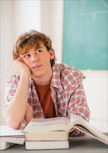 Teenage boy (14-15) sitting in classroom with pencil and books