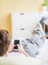 Teenage boy (14-15) lying on bed and text messaging
