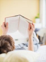 Teenage boy (14-15) lying on bed and reading book