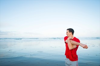 Young adult man stretching on beach