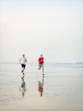 Young adult men running on beach