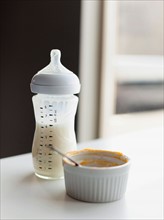 Milk in baby bottle and small bowl on table