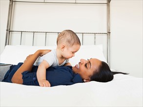 Mother holding her son (2-5 month), lying in bed happily