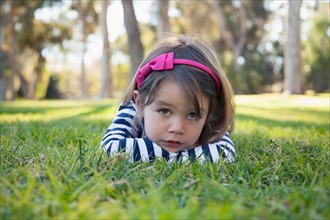 Portrait of sad girl (4-5 years) lying on grass in park