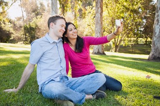 Couple sitting on grass in park photographing themselves