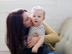 Portrait of mother sitting on sofa and kissing her daughter (12-17 months)