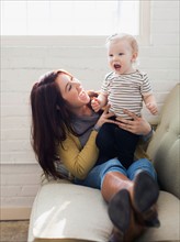 Mother and daughter (12-17 months) playing on sofa, Laughing and having fun