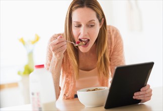 Woman eating breakfast and looking at tablet pc.
