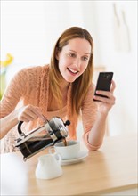 Woman pouring coffee and looking at phone.