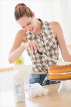 Woman decorating cake in kitchen.