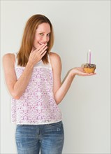 Studio portrait of woman holding birthday cupcake.