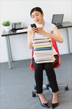 Businesswoman with stack of files texting on phone.
