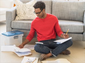Man sitting on floor in living room and calculating bills.