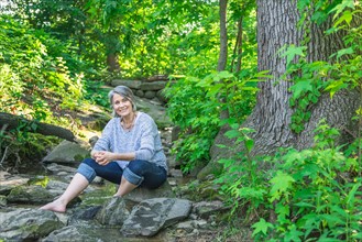 Central Park, New York City. Senior woman sitting on rock in forest.