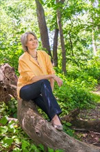 Central Park, New York City. Senior woman sitting on log in forest.