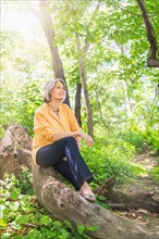 Central Park, New York City. Senior woman sitting on log in forest.