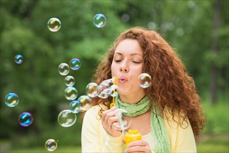 Young woman blowing bubbles in park.