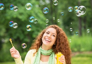 Young woman blowing bubbles in park.