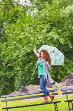 Woman with umbrella dancing on bench in park.