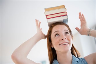Teenage girl (14-15) holding stack of books on head