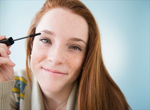 Teenage girl (14-15) applying mascara, studio shot