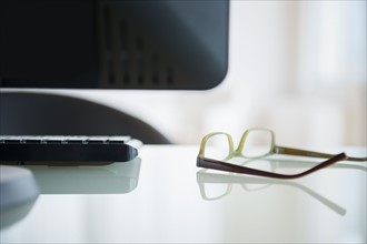 Glasses lying on desk near computer, studio shot