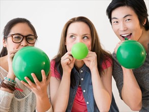 Portrait of young women and man blowing green balloons