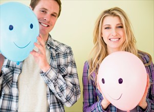 Studio shot of couple holding balloons with smiley faces