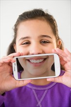 Studio shot of girl (8-9) holding smartphone with picture of her mouth
