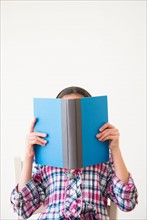 Studio shot of girl (12-13) hiding behind open book