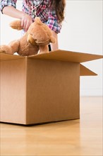 Girl (8-9) packing teddy bear to carton box