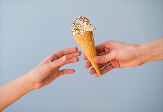 Hands passing ice cream against blue sky