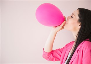 Young woman blowing pink balloon