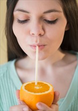 Young woman drinking orange juice from orange fruit