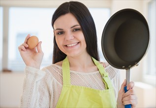 Young woman holding frying pan and egg