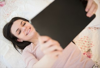 Portrait of young woman lying down on bed and holding digital tablet