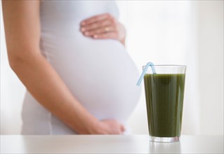 Mid section of pregnant woman, green smoothie in front