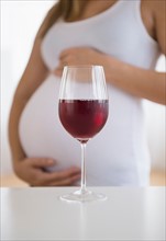 Mid section of pregnant woman, red wine in front