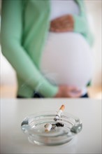 Mid section of pregnant woman, ashtray and cigarette in front