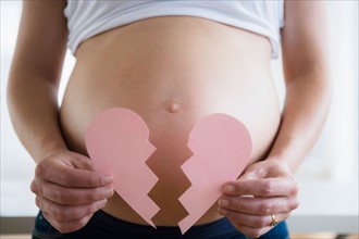 Mid section of pregnant woman holding broken paper heart