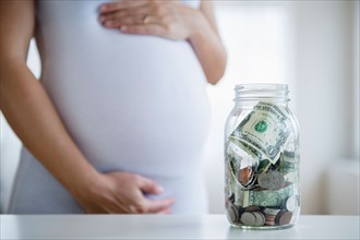 Mid section of pregnant woman, jar with money in front