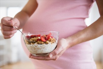 Mid section of pregnant woman holding bowl with granola