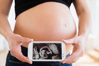 Mid section of pregnant woman holding mobile phone
