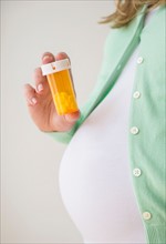 Mid section of pregnant woman holding pill bottle