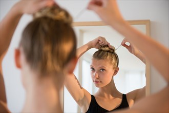 Rear view of teenage (16-17) ballerina looking into mirror and styling her hair