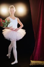 Teenage (16-17) ballerina on stage holding bunch of roses